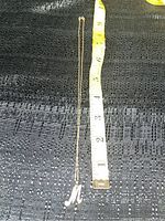 Necklace with 'M' pendant laid out next to a measuring tape showing length.