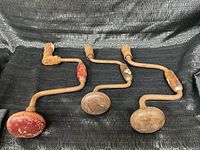 Lot of three antique hand drills laid out on black cloth, showing full view of drills.