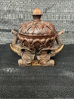 Front view of the elephant trinket box showing three elephants with raised trunks and the detailed dome lid with a clear faceted knob