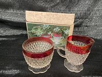Front view of the cream pitcher and sugar bowl with original box behind them. The pieces have a textured diamond point pattern and a ruby red band around the top.