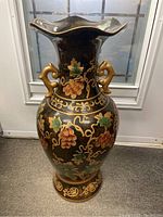 Front view of large black ceramic floor vase with grapevine painting, gold trim and sculpted handles.