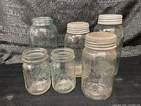 Wide angle photo showing all six vintage glass jars with white metal lids, varying sizes, one jar chipped at the top rim