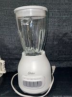 Full view of white Oster blender with clear glass jar and lid, showing overall condition and design.