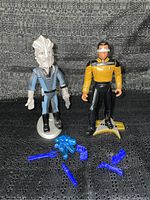 Two Star Trek figures displayed on a black fabric background with multiple blue plastic accessory pieces in front of them.