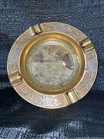 Full view of round brass ashtray showing floral-etched outer rim and four cigarette rests.