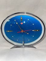 Front angle view of vintage mechanical blue oval alarm clock showing clock face, hands, and chrome base.
