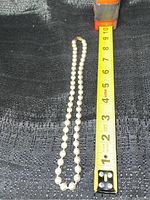 Full length of the pearl necklace shown alongside a measuring tape, measuring about 16 inches.