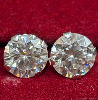 Close-up of pair of round moissanite stud earrings in 10K gold setting against red fabric background.