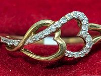 Close-up photo of 10K gold ring featuring intertwined heart design with natural diamond accents on red velvet background.
