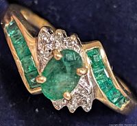 Angled top view showing central oval emerald flanked by channel-set princess-cut emeralds and cluster of round diamonds.