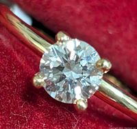 Close-up of round brilliant cut lab-grown diamond in four-prong setting on polished yellow gold band