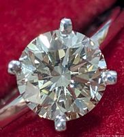 Close-up top view of round brilliant-cut diamond in six-prong setting against red background