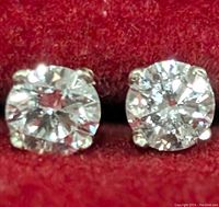 Close-up of the front side of two round cut lab-created diamond stud earrings showing clarity and sparkle on red velvet background.