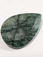 Loose faceted genuine emerald pear-shaped gemstone photographed on white background, showing front face with natural inclusions and color variation.