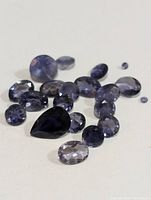 Photo showing a collection of various cut iolite gemstones spread out on a white background.
