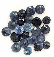 Close-up of approximately 25 small round faceted sapphires with varying blue tones and some inclusions visible.