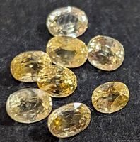 Close-up view of eight loose oval yellow sapphires displayed on a black fabric background to show color and cuts.