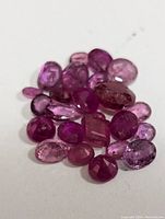 Close up photo of the loose natural ruby gemstones on a white surface showing various gem cuts and pink to red hues.