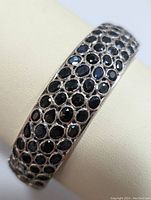 Front view of silver hinged bangle bracelet encrusted with multiple oval and round blue sapphires.