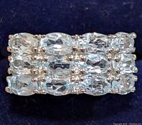 Close-up view of the ring face showing three rows of oval blue topaz stones in silver settings.