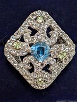 Top angled view of sterling silver ring showing cushion-cut blue topaz center, surrounded by small peridot and clear cubic zirconia stones in an ornate design.