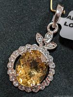 Close-up front view of silver pendant with oval yellow citrine stone and clear stone accents surrounding it and floral motif at top