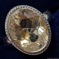 Close-up of silver ring with large oval faceted citrine gemstone showing twisted rope bezel detail