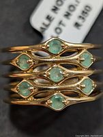 Close-up of gold-tone silver ring displaying eight small round green emerald stones in symmetrical open lattice design.