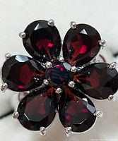 Close-up photo of the ring's garnet flower design showing six pear-shaped garnet stones and one central round garnet stone, all faceted with prong settings in silver.