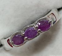 Close-up image of silver ring with three oval cabochon purple ruby stones set on top, front view