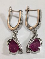 Front view of silver earrings with pear-shaped ruby and cubic zirconia accents
