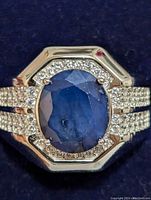 Close-up front view of silver ring featuring a central oval faceted blue sapphire surrounded by small round cubic zirconia stones on bezel and band.