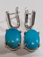 Front view of the pair of silver earrings with oval turquoise stones showing prong setting and clasp detail.