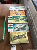 Top view of five boxed airplane model kits on table, showing brand names and artwork of aircraft models, including Huey Chopper and Junkers JU188.