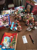 Overview of ceramic bisque bear figurines, boxed and loose vintage glass Christmas ball ornaments in red, green, gold, silver, string lights and Nutcracker Fantasy book on table