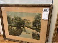 Photo of framed creek scene print with wooden frame and glass, showing creek with trees and reflections.