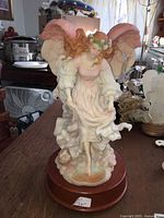 Front and slightly angled view of the large resin angel figurine music box showing pink wings, floral base, and wooden platform.