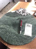 Top view of the round green marble platter showing metal fruit accent, pen, and lot tag for size reference.