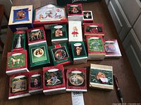 Photo of 20 boxed Hallmark Christmas ornaments arranged on brown wooden table including themes of bears, horses, children, fancy designs