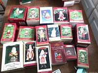 Photo showing 17 boxed Hallmark Christmas ornaments arranged on floor, each with image on box matching the contained Santa or Christmas figure ornament.