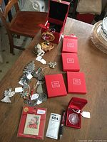 Photo of assortment of Christmas ornaments on wooden table including boxed Waterford Crystal snowflake, Lenox silver plated ornaments in red boxes, various silver plated ornaments with tags, and a Hallmark Lenox boxed ornament.