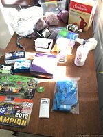 View of entire lot showing Kyle Busch NASCAR collectibles, yarn skeins, hourglass, hand lotion, egg shapers, steamer, potpourri, colored stones, and other small miscellaneous items on table.