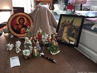 Photo showing the assembled ceramic Nativity set with various figures arranged alongside a circular wooden Jesus plaque and a framed picture of Jesus with angels.