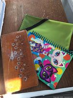 Photo showing a brown leather journal with floral embossed design, colorful cat art spiral notebook, and green zippered pouch on a wooden surface.
