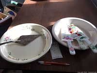 Two ceramic pie plates with three floral ceramic pie servers and one silver-plated embossed floral pie server presented on a wooden table.