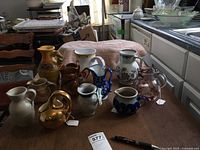 Overview of 10 assorted pitchers on wood table including ceramic and glass in various colors and designs