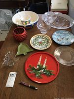 Photo of the full lot on a wooden table showing various Christmas themed platters, bowls, plates and tins in multiple colors and materials