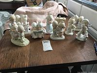 Photo showing 11 Precious Moments figurines arranged on a wooden table with a towel in background