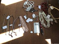 Photo showing a collection of various costume necklaces laid out on a wooden surface with a pen for size reference.