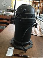 Full view of black theater can light standing upright on wooden table with attached power cord and mounting base visible.